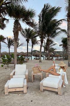 a woman sitting on top of a beach next to two white chairs and palm trees