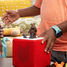 a woman is playing with a toy dinosaur on top of a red speaker box that's sitting on a table