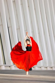 a woman in a red dress is dancing on the street with her arms up and hands behind her head