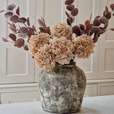 a vase filled with lots of flowers on top of a white table next to a door