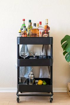 a bar cart with drinks on it next to a potted plant and other items