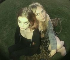 two young women sitting on the ground with their arms around each other's shoulders