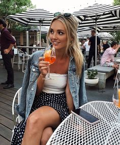 a woman sitting at an outdoor table holding a glass of orange juice in her hand