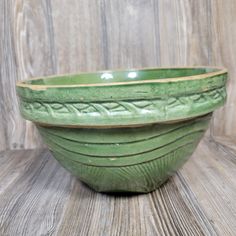 a green ceramic bowl sitting on top of a wooden table next to a wood wall