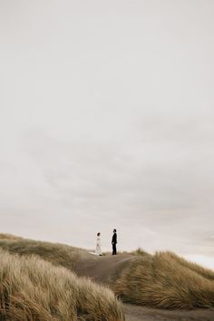 a man and woman standing on top of a grass covered hill