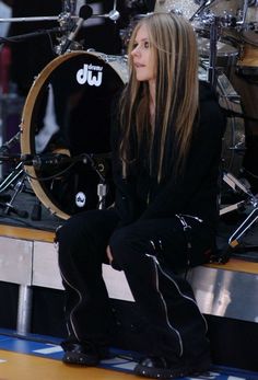 a woman sitting on top of a wooden bench next to a drum set in front of her