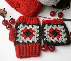 two crocheted red and black mitts next to cherries on a white surface