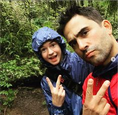 a man standing next to a young boy in the woods giving the peace sign with both hands