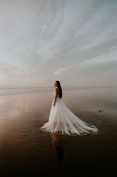 a woman standing in the water wearing a wedding dress