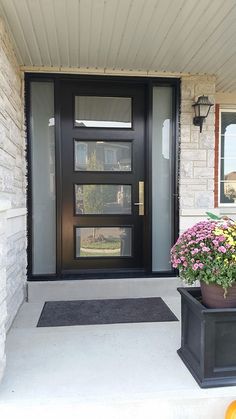 a black door and some flowers in front of it on a house's front porch