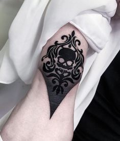 a black and white skull tattoo on the left arm with an ornate design around it