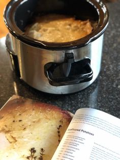 an open book sitting on top of a table next to a crock pot filled with food