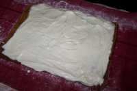 a square cake sitting on top of a red cloth covered table with white frosting