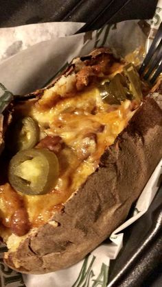 a close up of a baked potato with cheese and pickles on it next to a fork