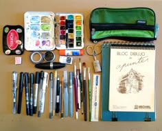 an assortment of art supplies laid out on top of a table next to a notebook