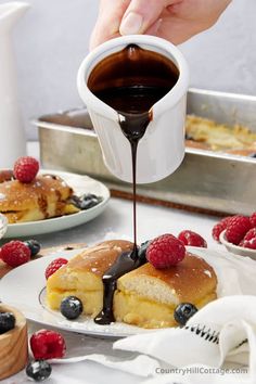 someone is pouring chocolate onto pancakes on a plate with raspberries and blueberries