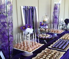 desserts are displayed on trays in front of purple and white decor at a party