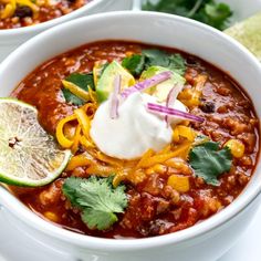 two bowls of chili with sour cream and cilantro garnish on top