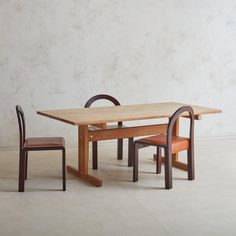 a wooden table and two chairs in front of a white wall with no one sitting at it