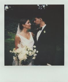 a man and woman standing next to each other in front of trees with white flowers