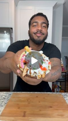 a man holding a doughnut with various toppings in his hands while standing next to a kitchen counter