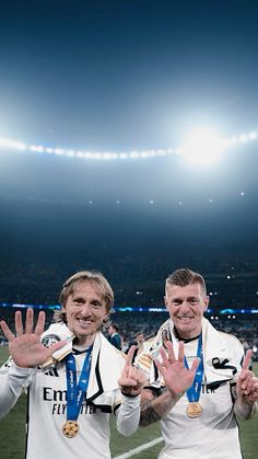 two soccer players holding their hands up in the air while standing on a football field