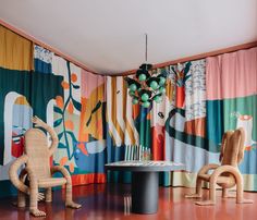 two wicker chairs and a round table in front of colorful curtained wallpaper