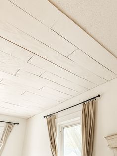 a bedroom with white walls and wooden ceilinging, along with curtains on the window sill