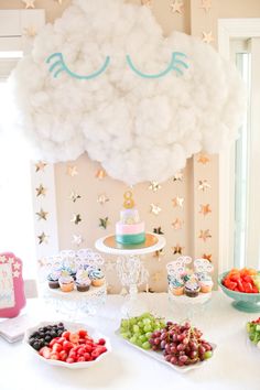 a table with cupcakes, fruit and other food on it in front of a cloud