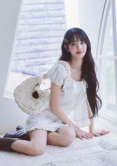 a woman sitting on top of a bed next to a window holding a stuffed animal