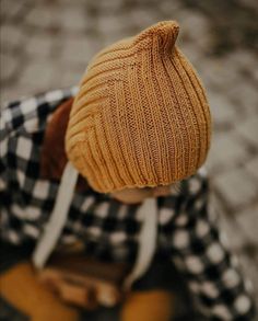 a young boy wearing a yellow knitted hat and plaid shirt, looking down at the ground