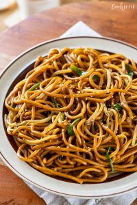 a white bowl filled with noodles and sauce on top of a wooden table next to a napkin