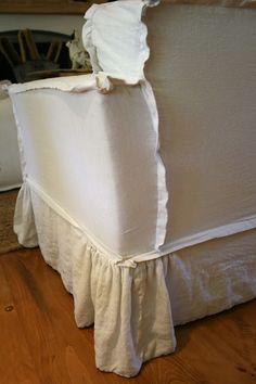 a white bed with ruffles on the top and bottom edge, sitting on a hard wood floor