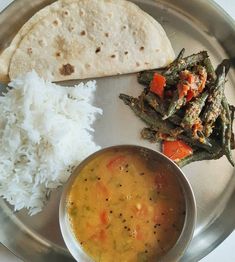 a silver plate topped with rice and vegetables next to a tortilla covered in sauce