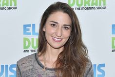 a woman with long brown hair and grey shirt smiling at the camera while standing in front of an event