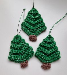 two crocheted christmas tree ornaments hanging from strings on a white surface with green yarn