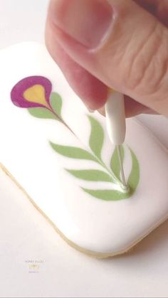 a hand holding a small white object with a purple flower painted on it's side