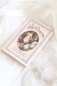 the little princess book is laying on a white bed sheet with pearls and beads around it