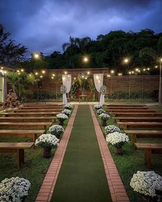 an outdoor ceremony setup with wooden benches and white flowers on the grass, surrounded by string lights