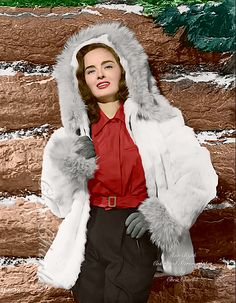 a woman wearing a fur coat and red shirt standing in front of a log wall