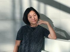 a woman leaning against a white wall with her hand on her chin and looking at the camera