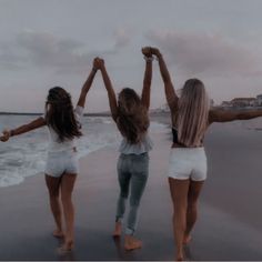 three girls are standing on the beach with their arms in the air