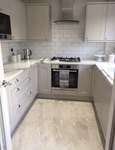 a kitchen with white cabinets and marble flooring, including an oven in the corner