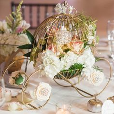 a birdcage filled with white flowers and greenery on top of a table