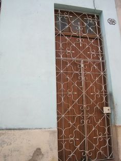 a wooden door with intricate iron work on the side of a blue building in an alleyway