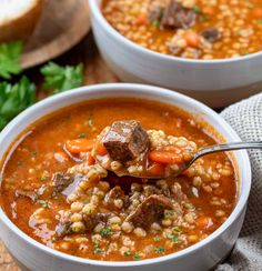 two white bowls filled with soup on top of a wooden table next to bread and garnished with parsley