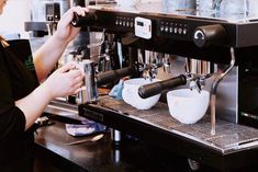 a woman working in a coffee shop with two cups on the espresso machine