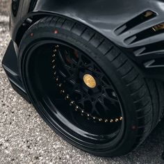 the front wheel of a black sports car with gold spokes and tire hubs