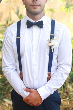 a man in a white shirt and blue suspenders is wearing a black bow tie