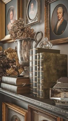 a shelf with books and pictures on it in front of some framed portraits, including an urn